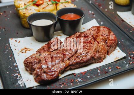 Una succosa carne alla brace bistecca con due salse siede su un quadrato nero piastra . Hot piatti a base di carne. Foto Stock