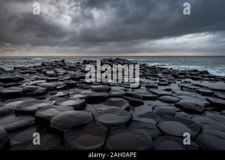 La naturale pietre esagonale al litorale chiamato Giant's Causeway, un punto di riferimento in Irlanda del Nord con drammatica cielo nuvoloso. Foto Stock