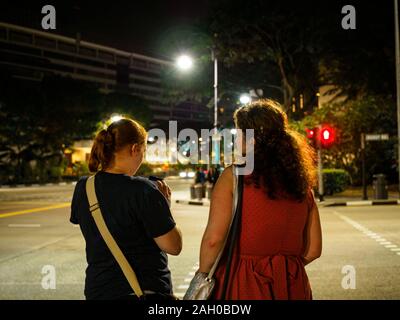 SINGAPORE - 17 MAR 2019 - Due giovani caucasici bianco le donne in attesa di attraversare la strada / strada in corrispondenza di un passaggio pedonale sul loro modo a casa la sera Foto Stock