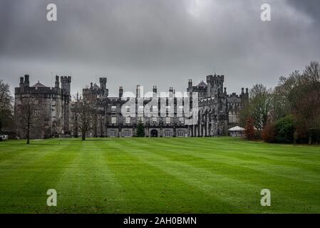 KILKENNY, Irlanda, dicembre 23, 2018: Castello di Kilkenny visto da un immenso giardino su un drammatico giorno nuvoloso con foglie secche sul prato verde. Foto Stock