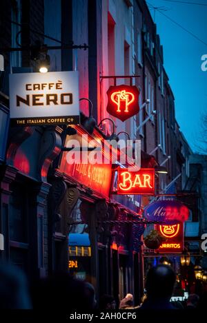 Dublino, Irlanda, dicembre 24, 2018: rosso brillante luci al neon, le indicazioni stradali e annunci di caffetterie, bar e ristoranti illuminare le persone a piedi Foto Stock