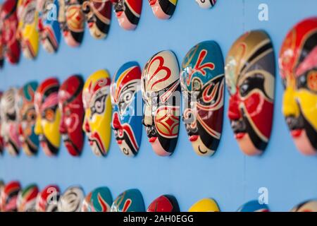 Colorato dipinto a mano opera cinese maschere riagganciare ordinatamente su una parete di blu. I vari colori ciascuna maschera rappresenta diverse caratteristiche. Foto Stock