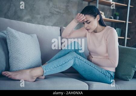 Foto del profilo della bella signora che soffre di periodo tenendo le mani sul ventre percossi e fronte divano indossare pullover e jeans in appartamento Foto Stock