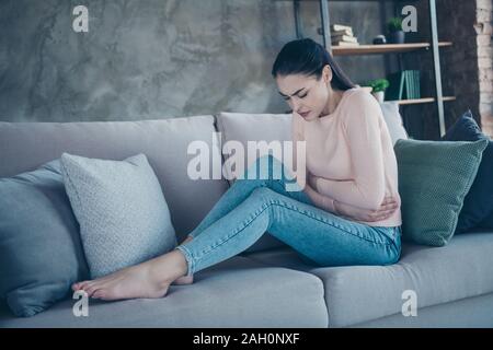 Foto del profilo di pretty lady affetti da pom tenendo le mani sul ventre percossi divano indossare pullover e jeans in appartamento Foto Stock