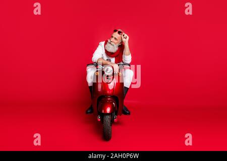 Lunghezza completa di foto pensieroso anziano toccando i suoi occhiali eyewear sedersi sulla bici pensare che indossa il ponticello bianco Pantaloni Pantaloni isolate su rosso Foto Stock