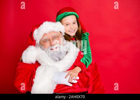 Close up foto di affascinante piccolo elf helper nel cappello verde headwear abbracciando piggyback suo divertente santa claus indossando occhiali occhiali isolate su Foto Stock