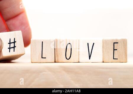 La parola amore su cubi di legno con Hashtag, close-up vicino a sfondo bianco Foto Stock
