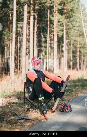 La formazione di un atleta sul rullo pattinatori. Il biathlon ride sul rullo di sci con bastoncini da sci, nel casco. Atleta è quasi pronto per iniziare. Autunno Foto Stock