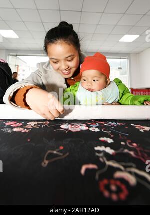 Guiyang, della Cina di Guizhou. Xxi Dec, 2019. Una donna che mantiene il suo bambino prende parte a un ricamo di formazione presso un sito di rilocazione in Congjiang County, a sud-ovest della Cina di Guizhou, 21 dicembre 2019. Credito: Yang Wenbin/Xinhua/Alamy Live News Foto Stock