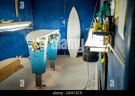 Tavole da surf essendo realizzati in un negozio con pareti blu e gli strumenti sui ripiani Foto Stock