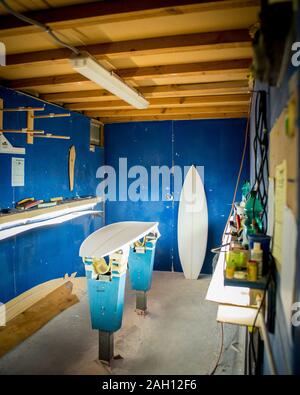 Tavole da surf essendo realizzati in un negozio con pareti blu e gli strumenti sui ripiani Foto Stock