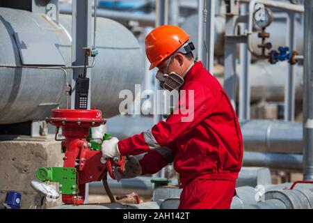 Lavoratore in rosso il lavoro di protezione usura e maschera a gas e indumenti da lavoro e casco arancione sul petrolio e gas impianto di raffineria. Foto Stock