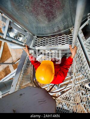 Lavoratore in rosso worwear e casco giallo sulla griglia grigia sulla raffineria di petrolio vegetale. Foto Stock