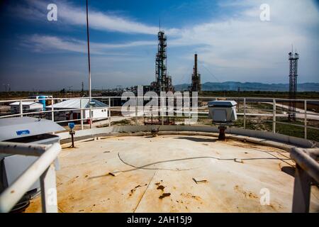 Grigio a colonna di distillazione su sole luminoso in corrispondenza di un cielo blu con nuvole sulla raffineria di petrolio pianta in un deserto. Foto Stock