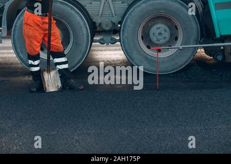 Asfaltatura. Lastricatore il lavoratore e la macchina su strada. La costruzione di nuove strade. Foto Stock