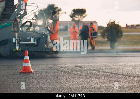 Asfaltatura. Lastricatore macchina e cono stradale e dei lavoratori. La costruzione di nuove strade. Foto Stock