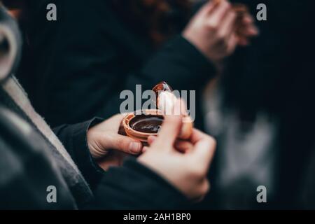 Donna mani di mangiare il cioccolato liquido sul mercato del cioccolato chocolART a Tubinga, Germania con natale stand e bancarelle con molte persone in piedi Foto Stock