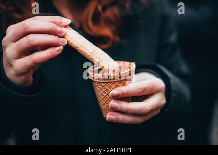 Donna mani di mangiare il cioccolato liquido sul mercato del cioccolato chocolART a Tubinga, Germania con natale stand e bancarelle con molte persone in piedi Foto Stock