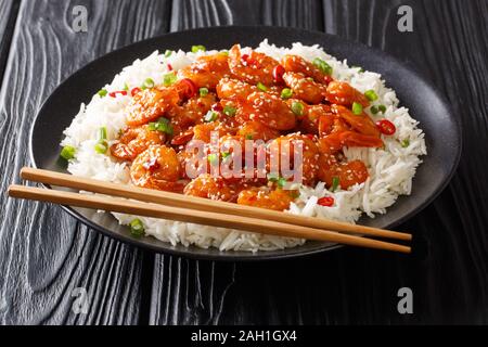 Asian Food gamberi fritti con aglio, peperoncino, i semi di sesamo e le cipolle verdi servito con riso close-up in una piastra su una tavola orizzontale. Foto Stock