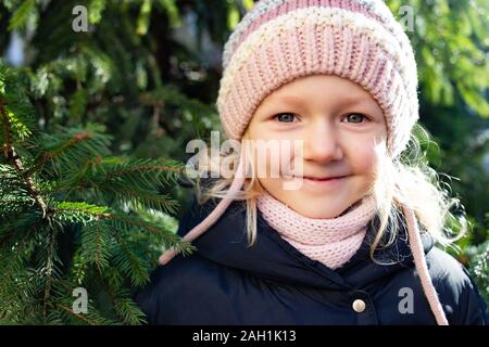 Poco bellissima ragazza con bel sorriso in posa in prossimità di abete in abiti casual Foto Stock