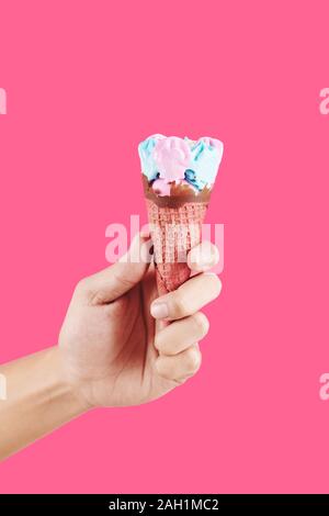 Mano con soft bubble gum gusto gelato in cialda di mais a caldo su sfondo rosa Foto Stock