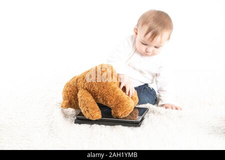 Studio di stock foto con uno sfondo bianco di un bambino che gioca con un tablet e un orso di peluche. Foto Stock
