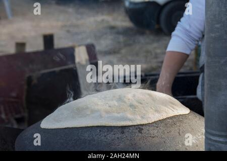 L'uomo la cottura di un tradizionale Drusi Pane Pita, su un Saj o Tava Foto Stock