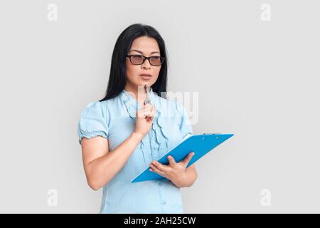 Freestyle. Donna asiatica in occhiali in piedi isolato su bianco con appunti e riflessivo della penna Foto Stock
