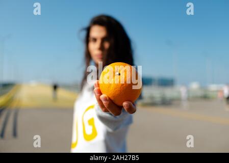 una ragazza in una felpa con cappuccio sportiva lancia un arancione come un baseball. Foto Stock