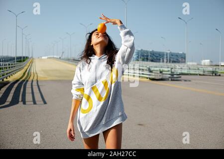 una ragazza in una felpa con cappuccio sportiva lancia un arancio come un baseball. sport, fitness Foto Stock