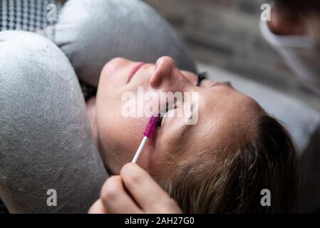 Cosmetologo pettini di ciglia di giovane donna caucasica. Ultimi ritocchi in processo di estensione delle ciglia. Procedure in un salone di bellezza, self-care. Foto Stock