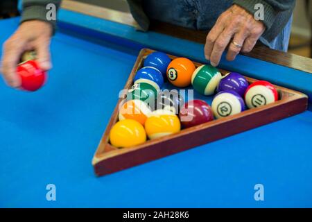 Le mani di un anziano uomo immissione delle palle di biliardo all'interno di un triangolo su un tavolo da biliardo. Foto Stock