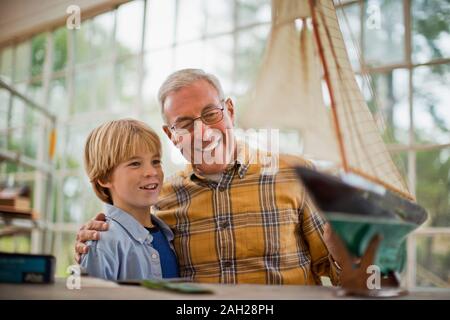 Soddisfatto senior l uomo e il suo nipote guardando la barca giocattolo hanno costruito insieme. Foto Stock