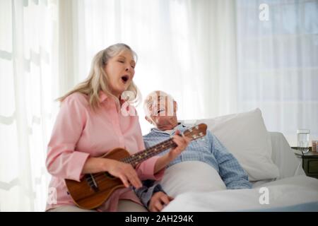 Donna matura a suonare la chitarra e cantare al suo marito anziano Foto Stock