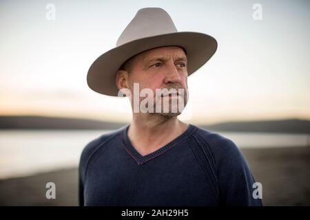 Ritratto di un uomo di mezza età che indossa un cappello da cowboy sulla spiaggia al tramonto Foto Stock