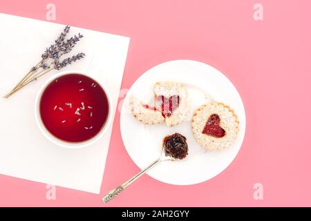 A forma di cuore i cookie e la tazza di tè lavanda, vicino, direttamente dal di sopra sulla luce sfondo rosa Foto Stock