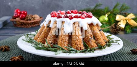 Natale torta di frutta sulla piastra bianca. Torta di frutta fatta in casa decorata con rosmarino, lo zucchero in polvere e lingonberry su una tavola di legno sfondo rustico Foto Stock