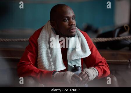 I giovani africani sportsman seduta sul banco e acqua potabile egli riposo dopo la formazione sportiva Foto Stock