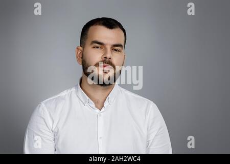 Calma bello uomo barbuto pone in studio su sfondo grigio Foto Stock
