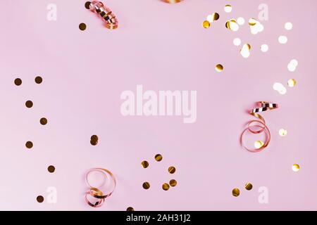 Shiny golden confeti e nastri su sfondo rosa. Cornice festosa. Foto Stock
