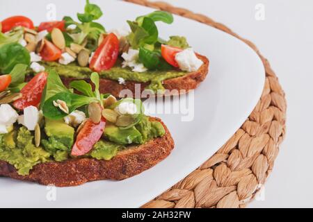 Due pane di segale brinda con purea di avocado, i pomodori e il formaggio feta. Antipasto sano sulla piastra bianca di close-up Foto Stock