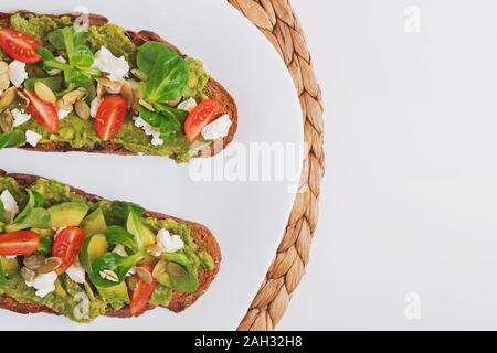 Due pane di segale brinda con purea di avocado, i pomodori e il formaggio feta. Antipasto sano sulla piastra bianca, vista dall'alto Foto Stock