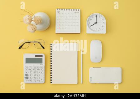 Notebook, mouse, telefono, calcolatrice, bicchieri, penna, calendario, allarme su sfondo giallo. Flatlay, vista dall'alto. Foto Stock