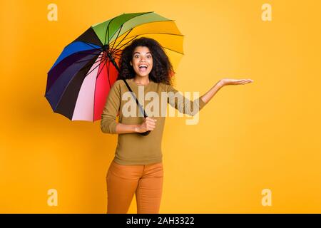 Foto di allegra positivo marrone carino nizza piuttosto affascinante ragazza dolce azienda oggetto con le mani mentre cattura le gocce di pioggia indossa pantaloni pantaloni arancione Foto Stock