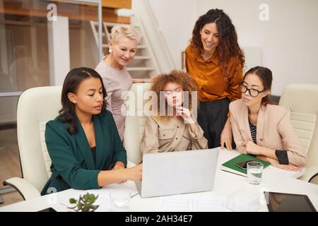 Cinque successo etnicamente diverse donne di diverse età guardare qualcosa sul computer portatile in ufficio inquadratura orizzontale Foto Stock