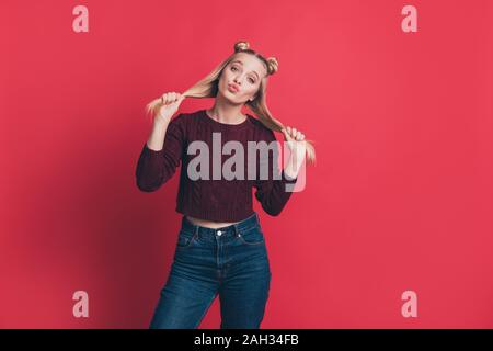 Foto della bella signora di inviare aria baci tenendo i capelli lunghi in mani flirty mood usura borgogna maglia pullover e jeans isolato di color pastello di colore rosso Foto Stock