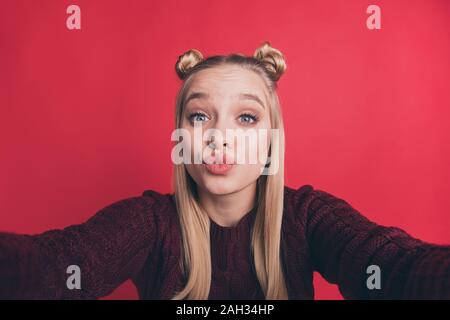 Primo piano della bella signora funny gioventù acconciatura rendendo selfies inviare aria baci ai seguaci indossare borgogna pullover a maglia isolato rosso pastello Foto Stock