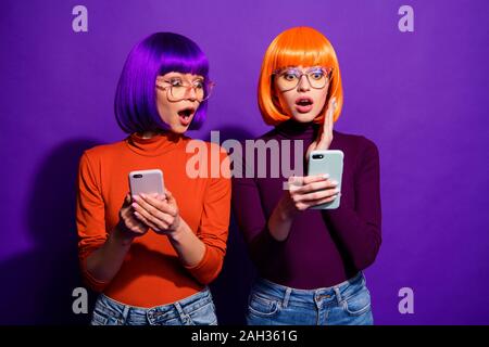 Ritratto di due belle attraente bella carino Allegro vivace stupiti le ragazze in parrucche utilizzando una cella per leggere le notizie guardare i media isolate su bright vivid Foto Stock