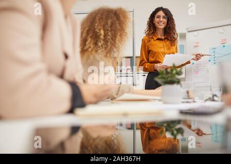 Elegante adullt giovane imprenditrice con lunghi capelli ricci azienda presentazione a office meeting, inquadratura orizzontale Foto Stock