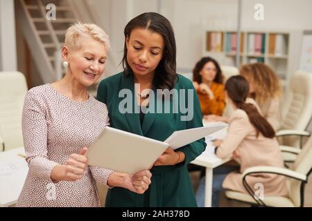 Donna matura che mostra qualcosa sul suo computer tavoletta al suo collega più giovane inquadratura orizzontale Foto Stock